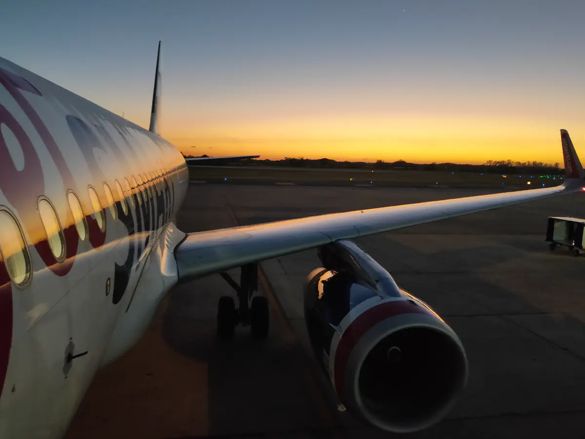 滑走路に駐機するJetSMART航空機のエンジンと翼。地平線にオレンジ色の夜明けが広がる
