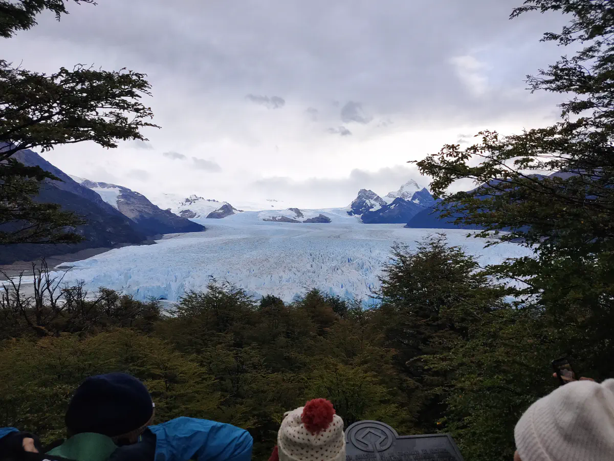 木々の隙間越しに見たペリトモレノ氷河の全景と奥の山並み