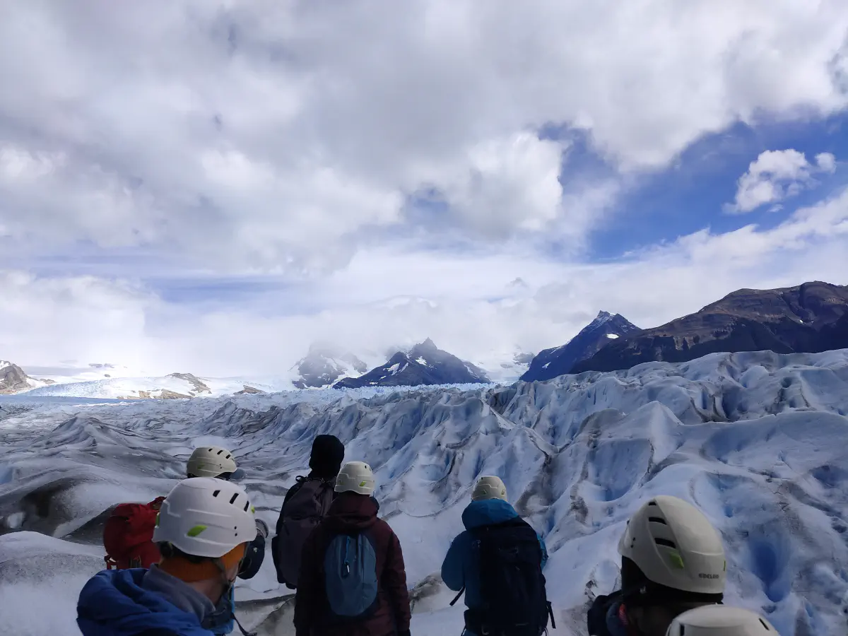 ヘルメットをかぶったトレッキング参加者たちが氷原に立ち、遠くの山々と氷河を眺めている