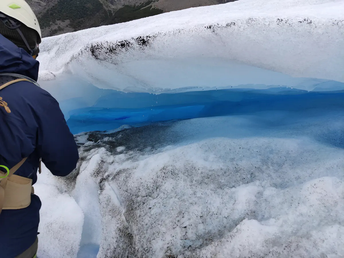 氷河の縁に立ち青い層の見える段差状のくぼみを見下ろす参加者