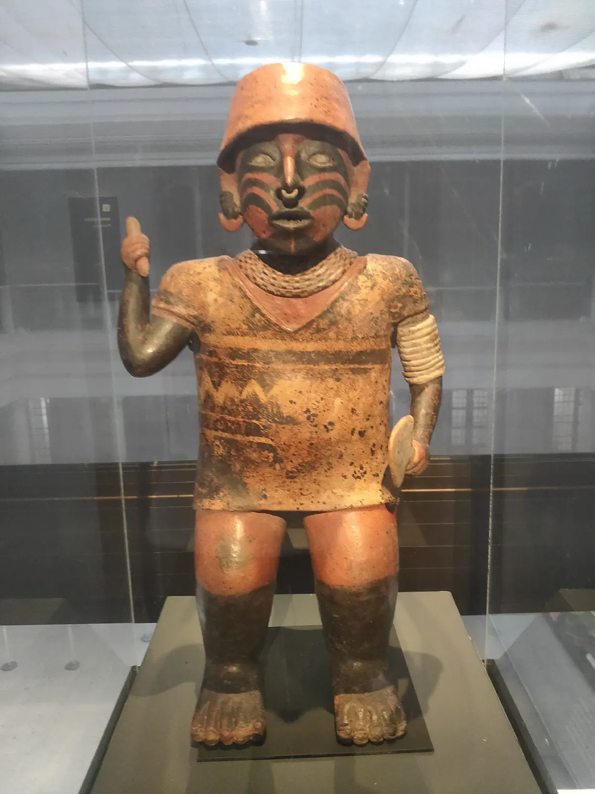 赤い帽子をかぶり顔に縞模様のペイントをした先コロンブス期の彩色土偶。全身像